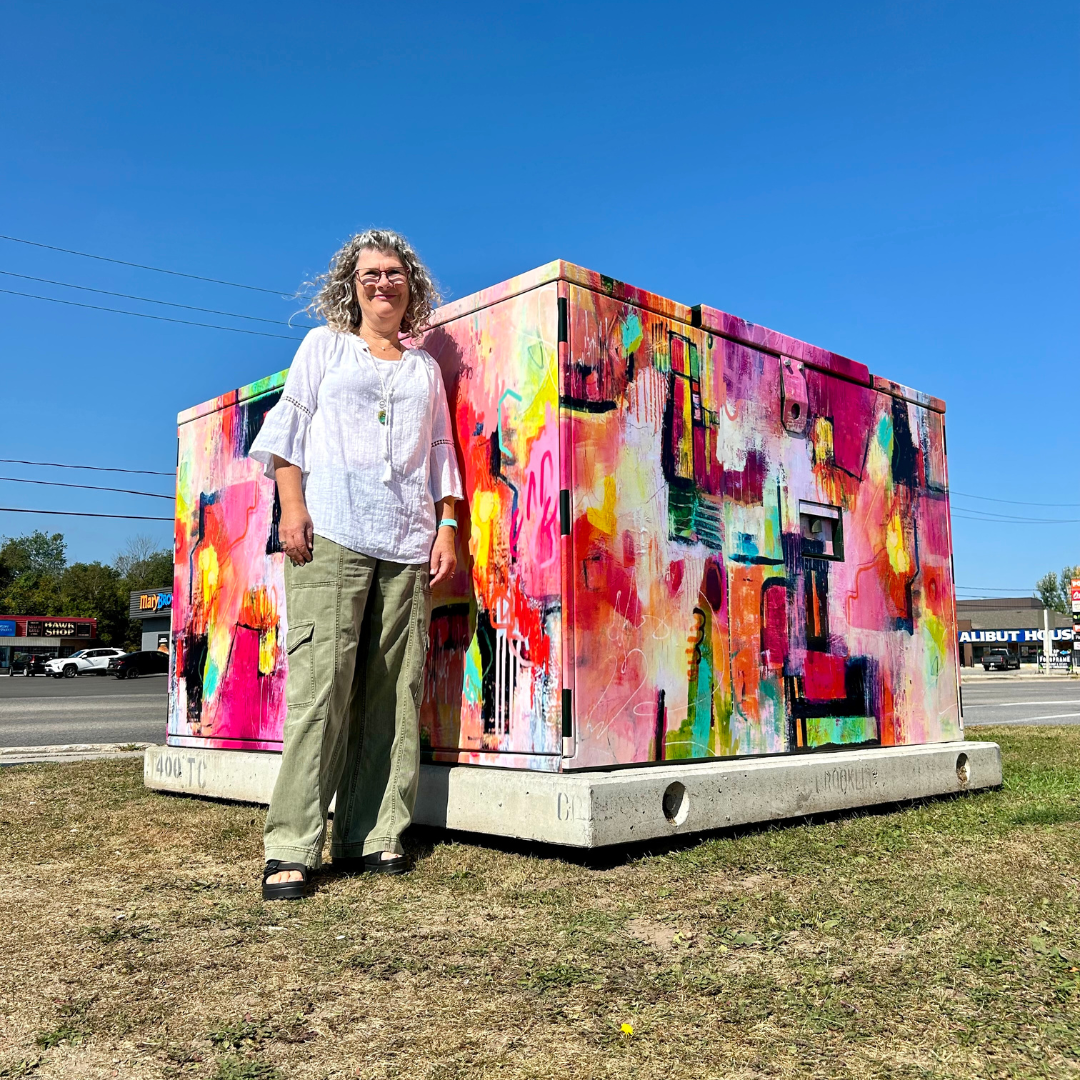 A woman stands in front of a hydro transformer wrapped in abstract art.